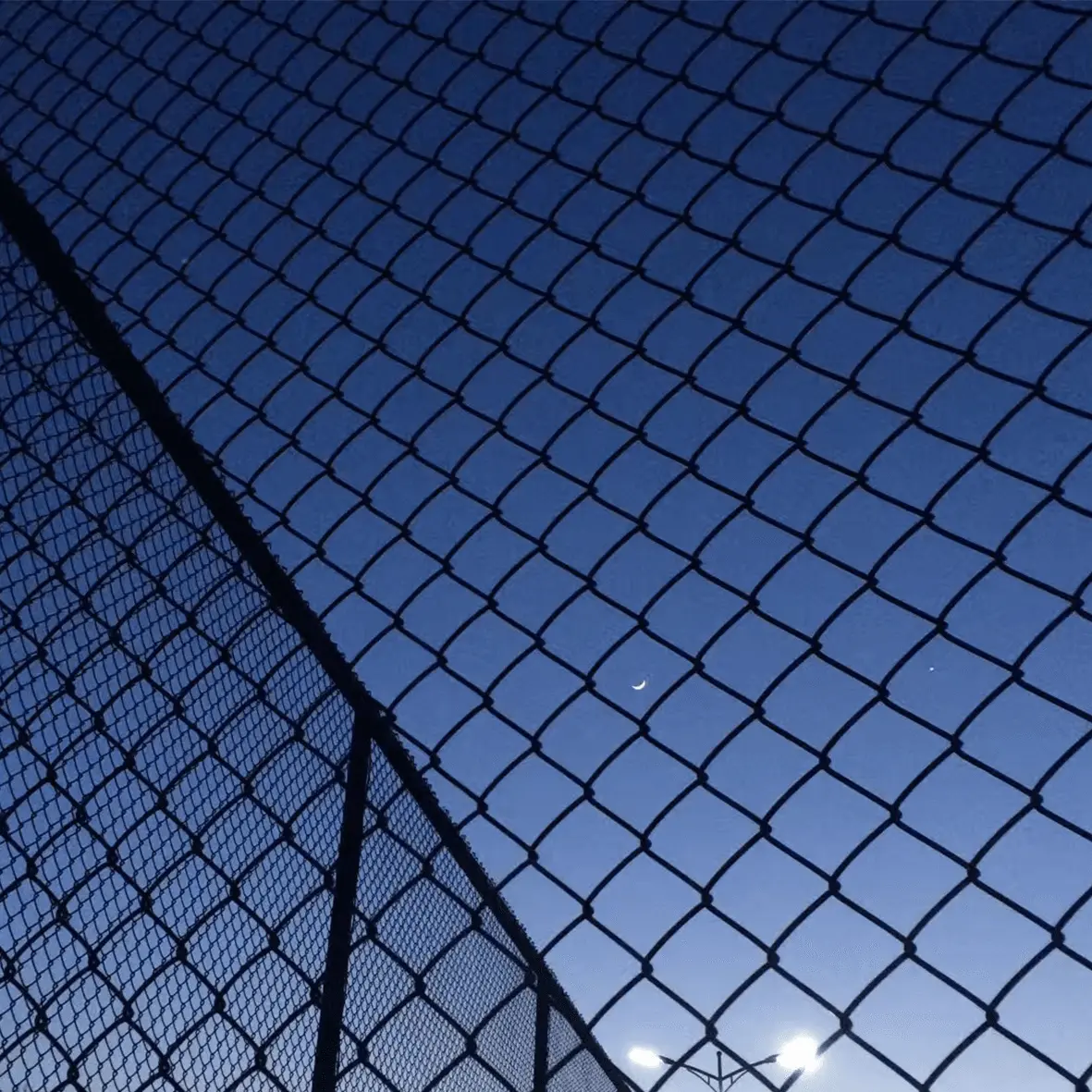Clear night sky through chain-link fence with moon visible
